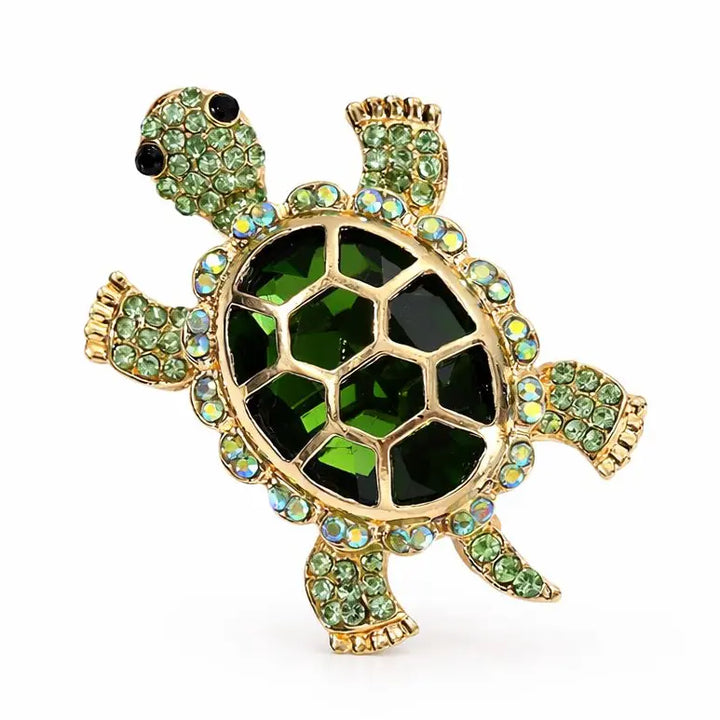 Decorative turtle brooch with green gemstones on a white background