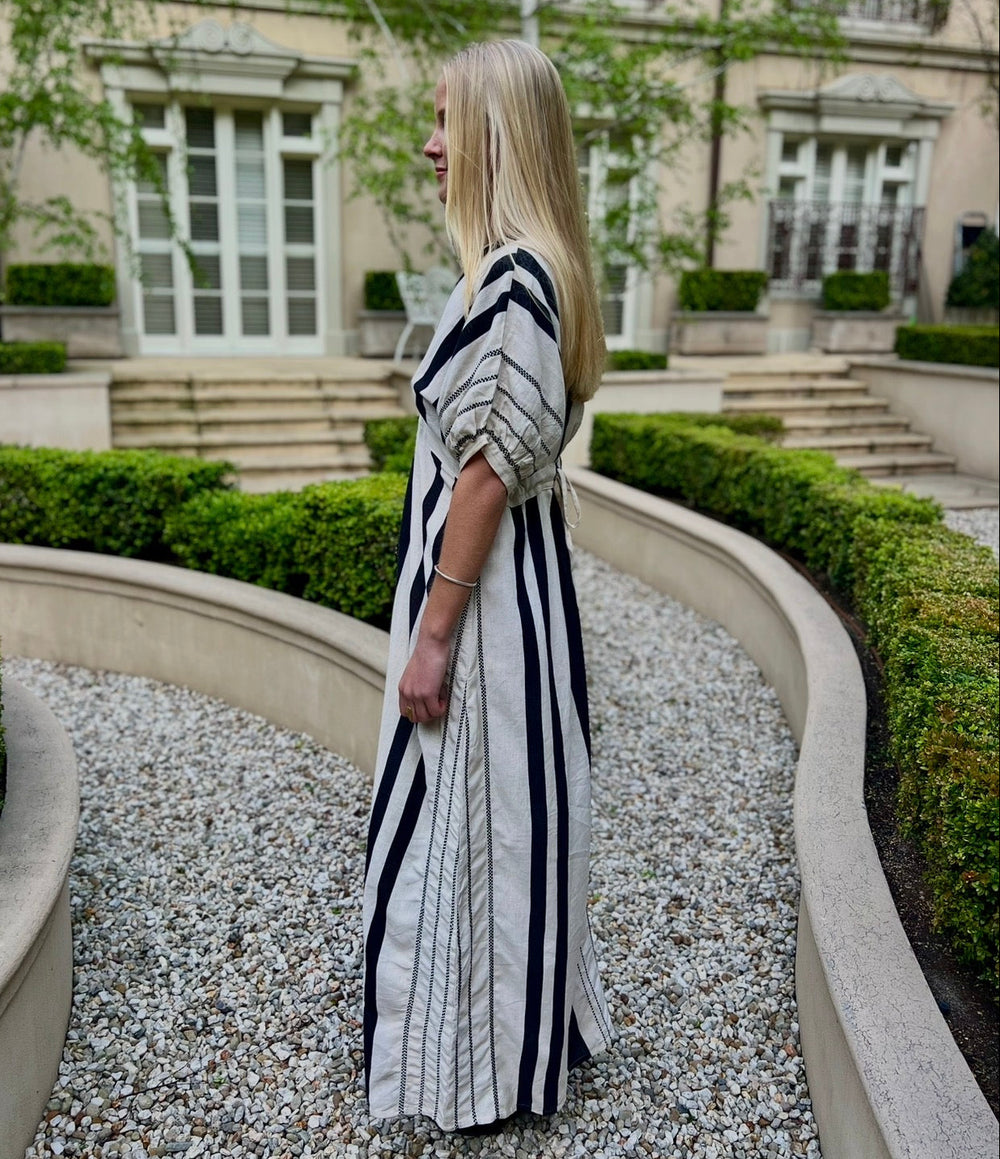 Woman in a black and white striped dress standing in a garden with a building in the background