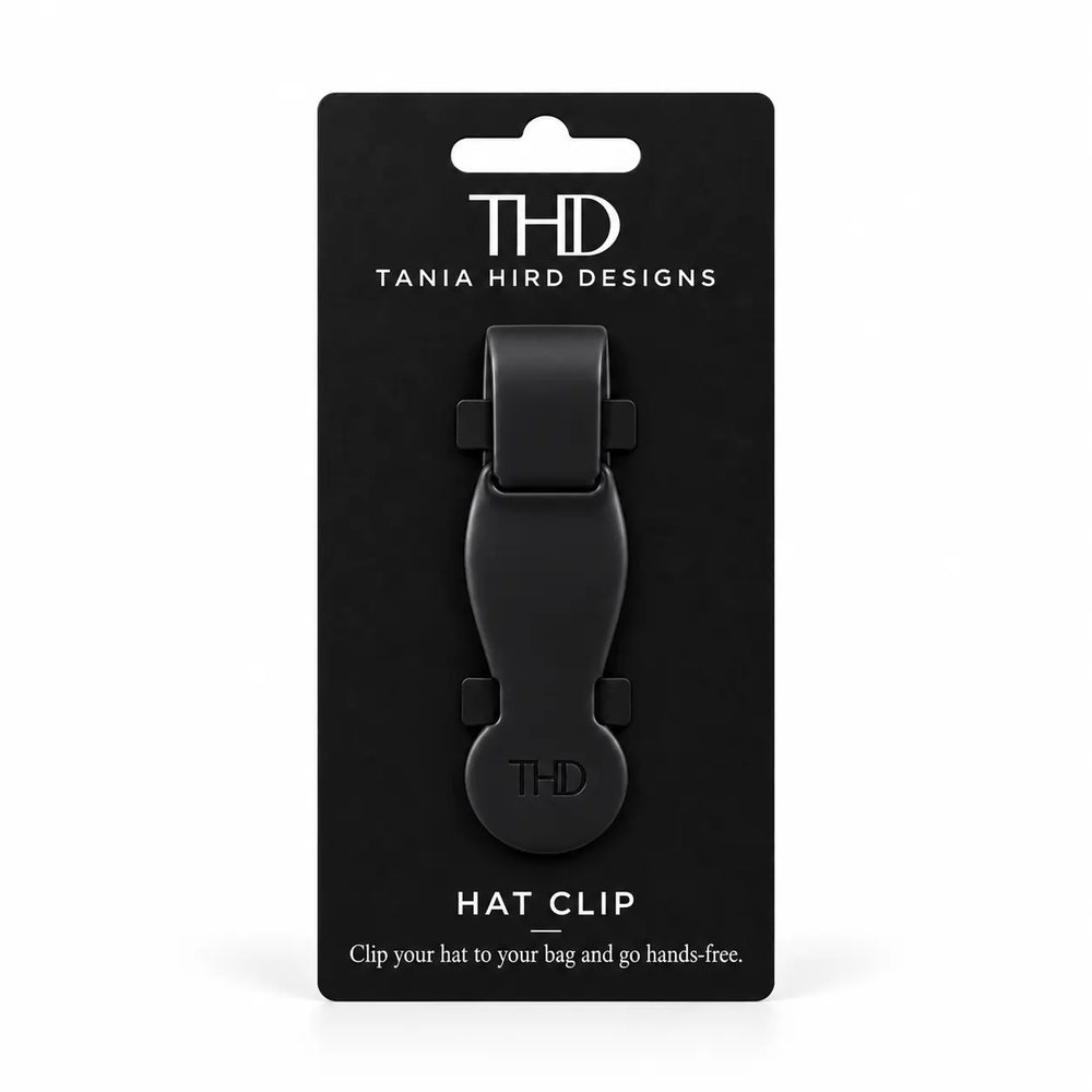 A black Tania Hird Designs hat clip mounted on a black retail card package, photographed against a plain white background.